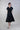 Look editorial con vestido midi de cintura fruncida y detalle escultórico, estilizado en clave contemporánea que resalta su construcción y fluidez.
